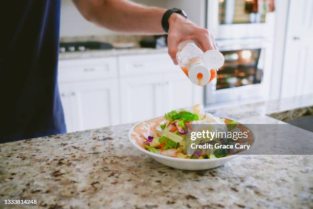 man pours salad dressing onto salad - molho vinagrete imagens e fotografias de stock