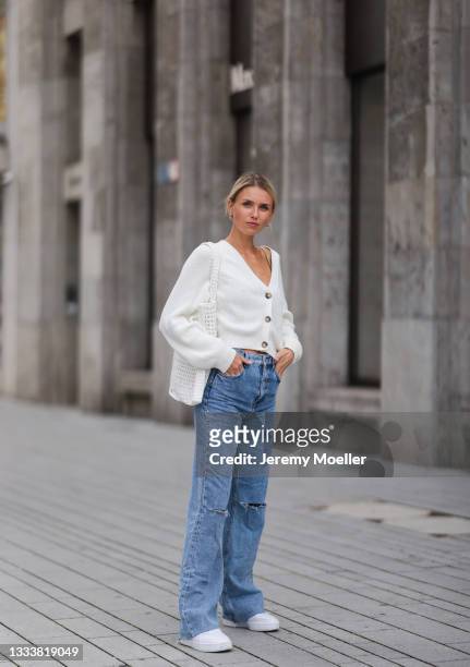 Scarlett Gartmann wearing Zara destroyed blue jeans, Prada white bag, beige Monki knit cardigan and Puma white sneakers on August 07, 2021 in...
