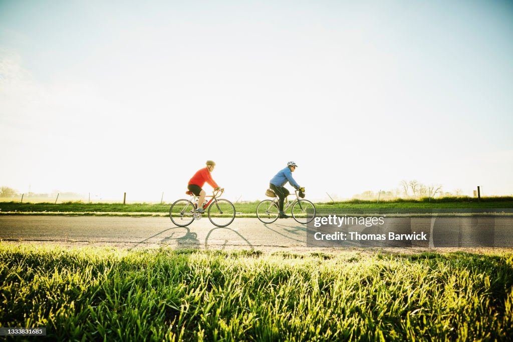 Wide shot of senior male friends on sunrise bike ride on rural road