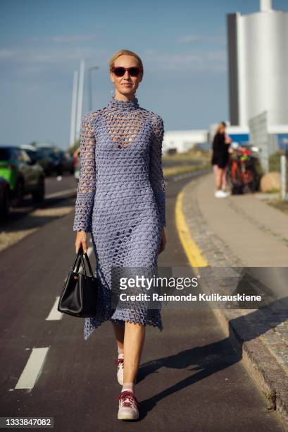 Guest wearing purple knitted dress and sneakers outside Ganni during Copenhagen fashion week SS22 on August 12, 2021 in Copenhagen, Denmark.