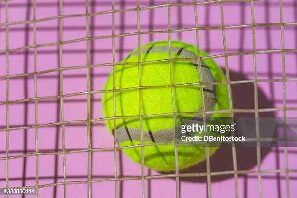 yellow tennis ball with focused hard shadow, under the string of a racket on pink background - abstract tennis player stock pictures, royalty-free photos & images