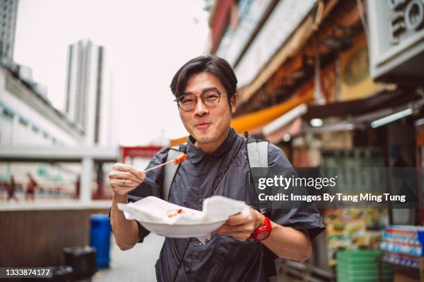 young handsome man enjoying hong kong local street food joyfully in street - chinese people posing for camera fotografías e imágenes de stock