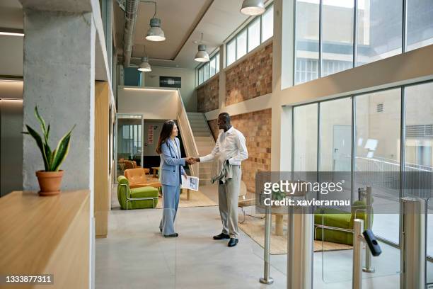 female real estate agent and male client shaking hands in greeting - conference lobby stock pictures, royalty-free photos & images