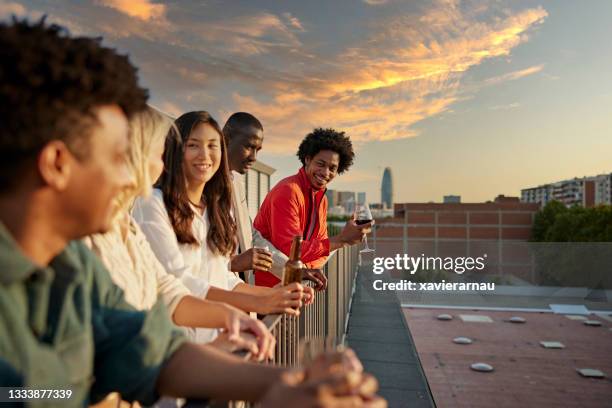 compañeros de trabajo relajándose con bebidas después del trabajo en la cubierta de la azotea - sunset freinds city fotografías e imágenes de stock