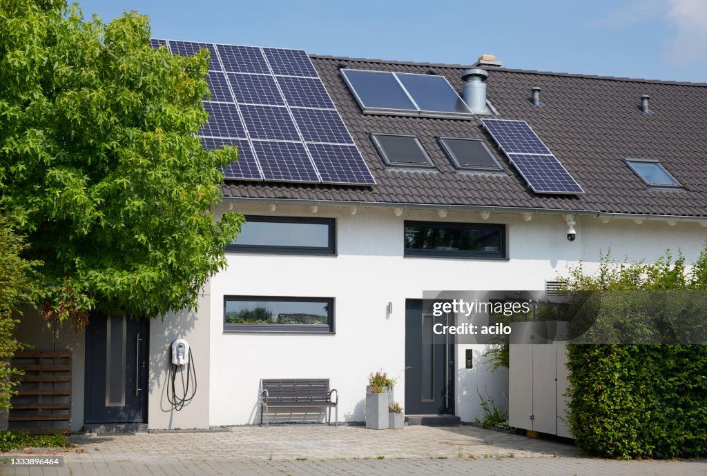 Moderna casa unifamiliar blanca con paneles solares y estación de recarga