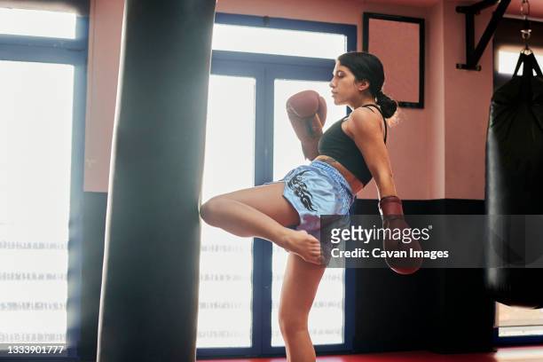 woman trains with a punching bag in a muay thai gym - kickboxing gloves stock pictures, royalty-free photos & images