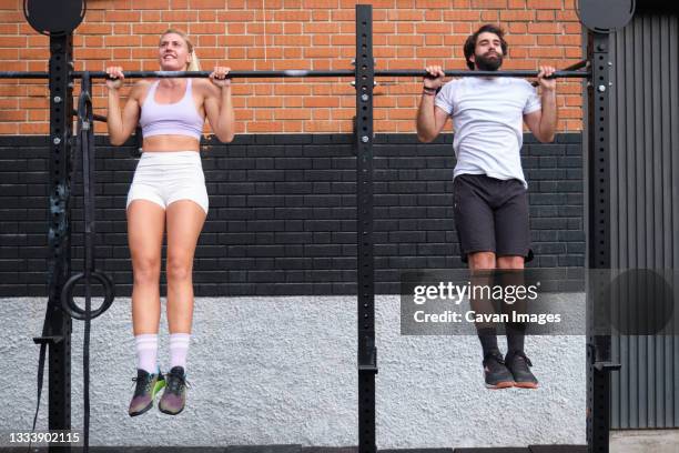 young man and woman doing pull ups at a crossfit pull up bar - sicherheitsgitter stock-fotos und bilder