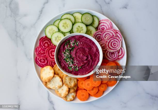 bowl of beet hummus, vegetables and crackers on white marble counter. - beet stock pictures, royalty-free photos & images