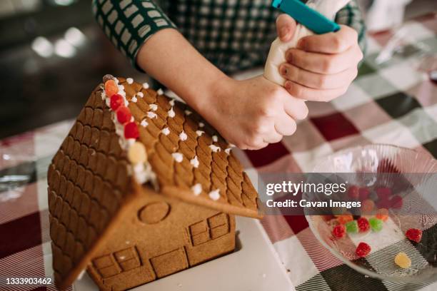 young girl decorating a ginger bread house at a table - gingerbread house stock-fotos und bilder