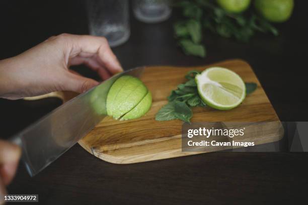 crop of hand, knife and sliced lime on the wooden board - fines herbes stock-fotos und bilder