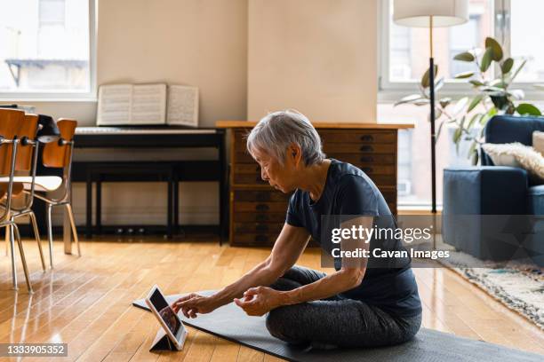 senior woman using digital tablet while exercising in living room - laminat stock-fotos und bilder
