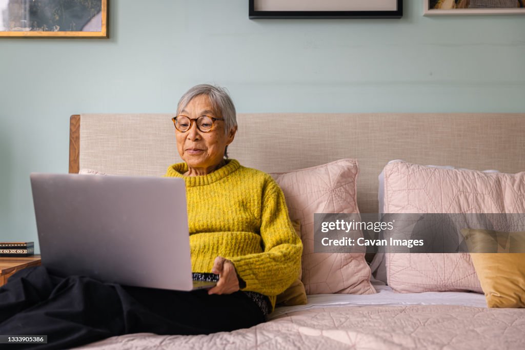 Senior asian woman using laptop while sitting in bedroom at home