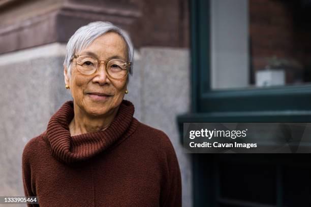 portrait of smiling senior woman wearing glasses in the city - elderly asian foto e immagini stock