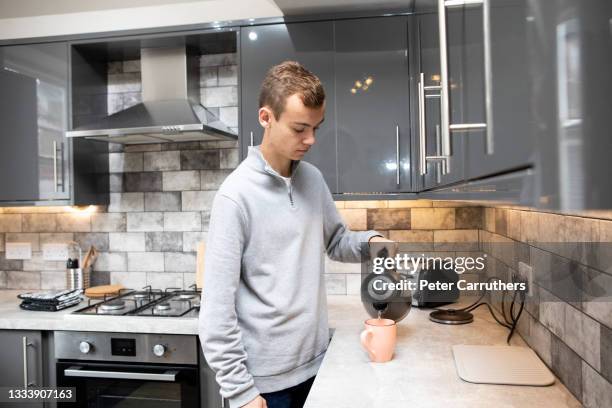 male university student making tea at a kitchen counter, pouring water from a kettle into a mug - kettle stock pictures, royalty-free photos & images
