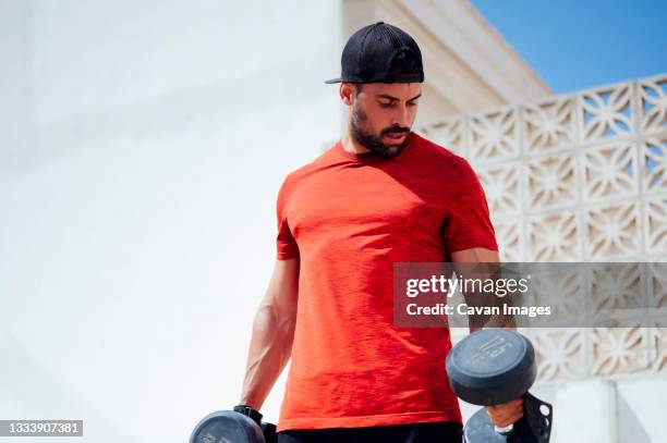 muscular young man lifting weights outside - over shoulder man stockfoto's en -beelden