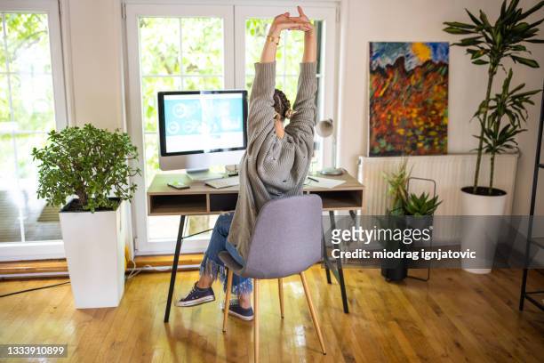 young woman stretching while telecommuting from home - back stretch stockfoto's en -beelden