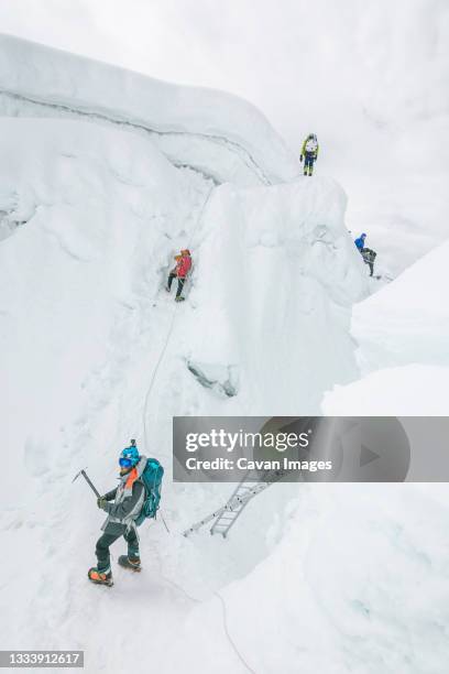 rope team navigating a big crevasse in the himalayas - cascade gelée photos et images de collection
