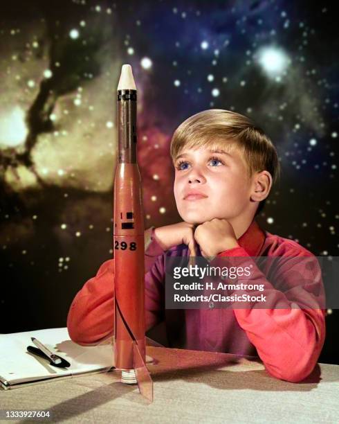 1960s Day Dreaming Boy With Model Rocket And Outer Space Background .