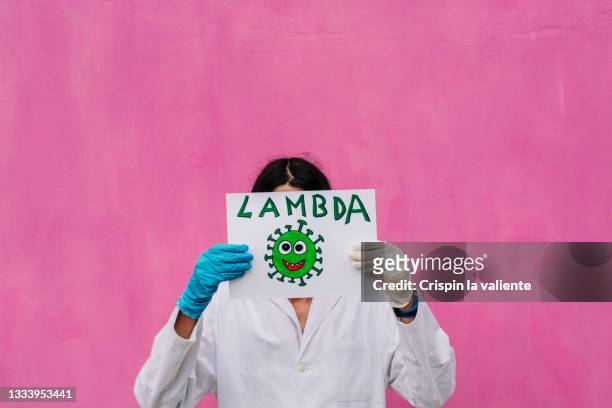 female scientist in lab coat holding funny sign with word lambda, covid - lambda phage stock pictures, royalty-free photos & images
