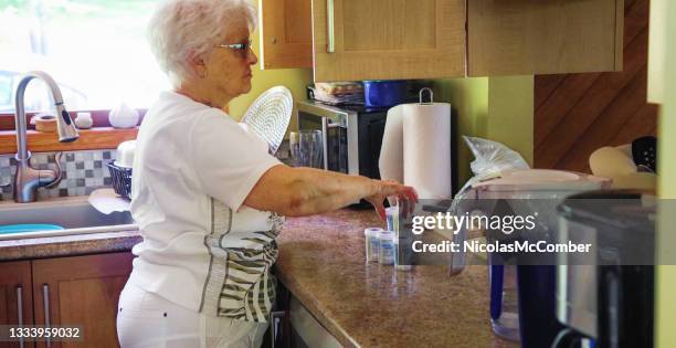 side view of senior female organizing her prescription drugs on her kitchen counter - prescription drugs dangers stock pictures, royalty-free photos & images