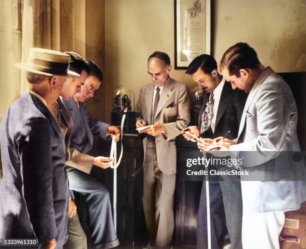 1930s Anonymous Brokers Investors Businessmen Reading Ticker Tape As It Comes Out Of Glass Domed Machine .