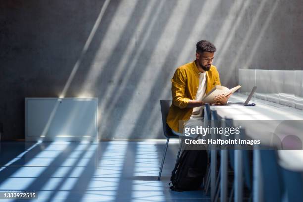 young university student with book indoors in librabry, reading. - exam desk stockfoto's en -beelden