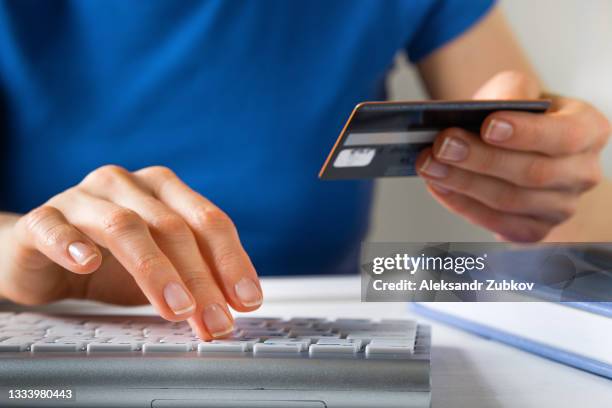 a woman is holding a credit card, typing on a laptop keyboard. there's a notepad and a pen next to it. the concept of buying online, ordering products at home, and paying via the internet. - russia internet stock pictures, royalty-free photos & images