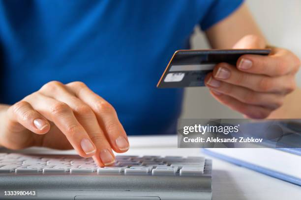 a woman is holding a credit card, typing on a laptop keyboard. there's a notepad and a pen next to it. the concept of buying online, ordering products at home, and paying via the internet. - moneytransfer stock pictures, royalty-free photos & images