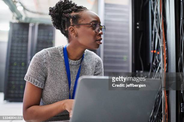 shot of a young woman using a laptop in a server room - profissional de informática imagens e fotografias de stock