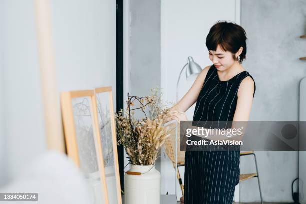 jeune femme asiatique décorant et disposant un vase avec des plantes séchées sur l’armoire dans le salon à la maison - arts culture and entertainment photos et images de collection