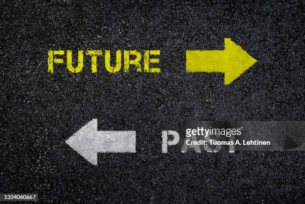 "future" and "past" signs/words with arrows pointing on opposite directions on dark, wet black asphalt road, top view. - with new era stock pictures, royalty-free photos & images
