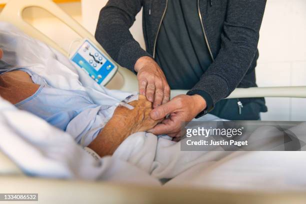 adult son comforts elderly mother in hospital - iv drip womans hand fotografías e imágenes de stock