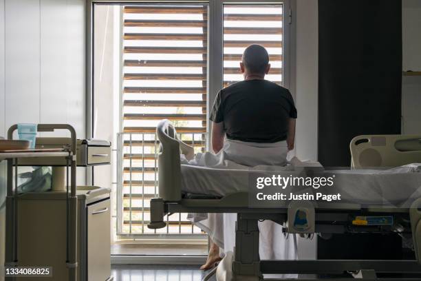 unrecognisable man sits on hospital bed and looks out of the window - unrecognizable person stock pictures, royalty-free photos & images