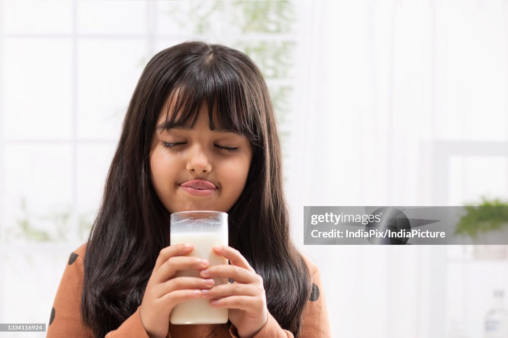 A YOUNG GIRL HOLDING GLASS OF MILK AND DRINKING
