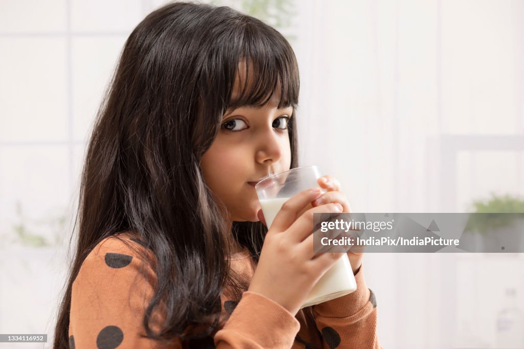 A YOUNG GIRL LOOKING AT CAMERA WHILE DRINKING MILK