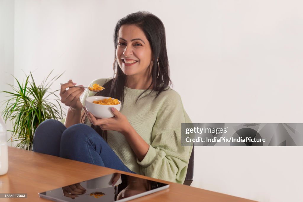 A CHEERFUL ADULT WOMAN SITTING IN FRONT OF CAMERA WITH A BOWL OF CORNFLAKES
