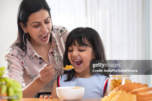 a happy daughter cheerfully eating cornflakes given by mother - rusk stock pictures, royalty-free photos & images