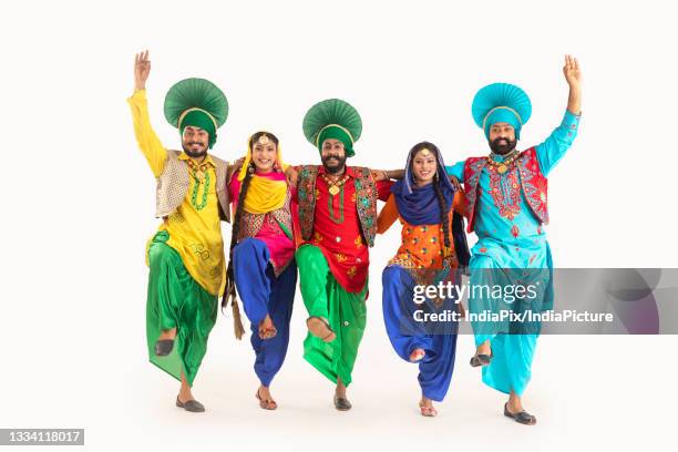 a troupe of punjabi folk dancers dressed in costume striking a dance step in unison. - bhangra fotografías e imágenes de stock