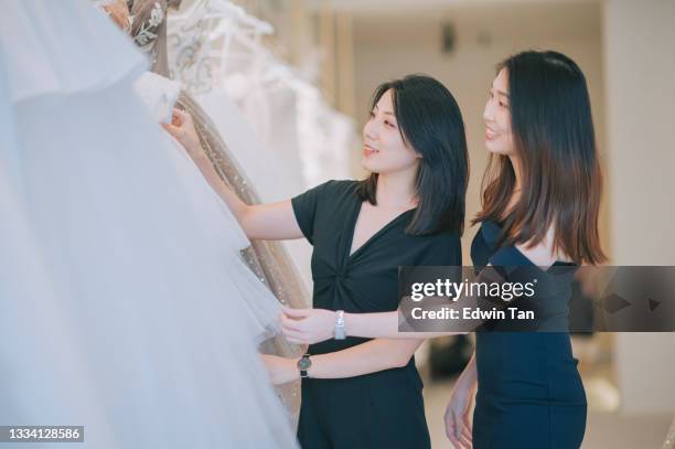 sposa e damigella asiatica cinese in cerca di abito da sposa perfetto per il giorno del suo matrimonio al negozio nuziale - wedding planning foto e immagini stock