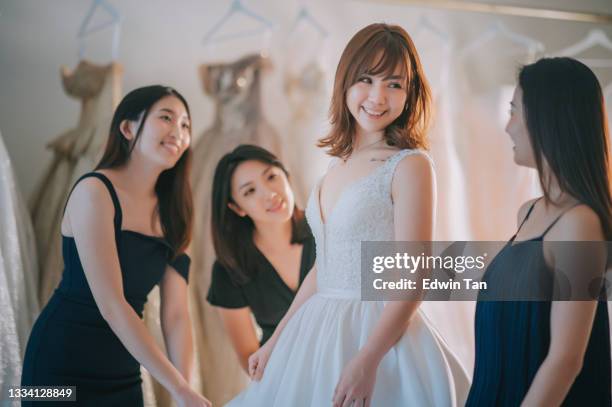 asiatische chinesische braut probiert brautkleid umgeben von brautjungfer bewundern die schönheit des brautkleides im brautladen - bridesmaid dress stock-fotos und bilder