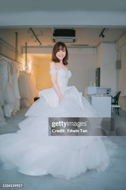 happy proud satisfied asian chinese bride portrait posing looking at camera smiling at bridal shop trying on wedding dress grown - wedding dress on hanger stock pictures, royalty-free photos & images