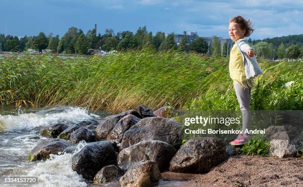 a 6-year-old caucasian girl stands on the shore of the lake and looks into the distance. a strong wind blows over the child's face and she loves it. - riet stockfoto's en -beelden