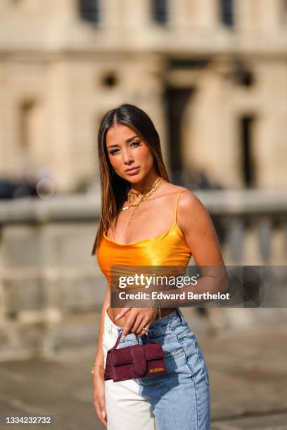 Isabeau Delatour @isabeau.delatour wears large gold chain pendants necklaces, a yellow V-neck cropped tank-top, gold large chain bracelets, a silver...