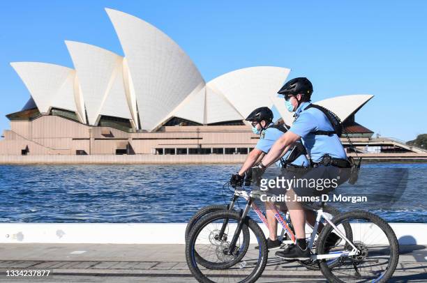 New South Wales police officers wearing face masks ride mountain bikes as they patrol to ensure public compliance at Circular Quay on August 15, 2021...