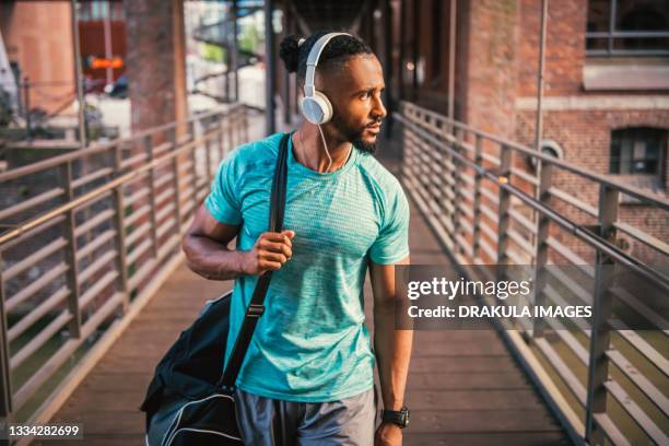 active young man, walks the city with gym bag and headphones - music city walk stock pictures, royalty-free photos & images