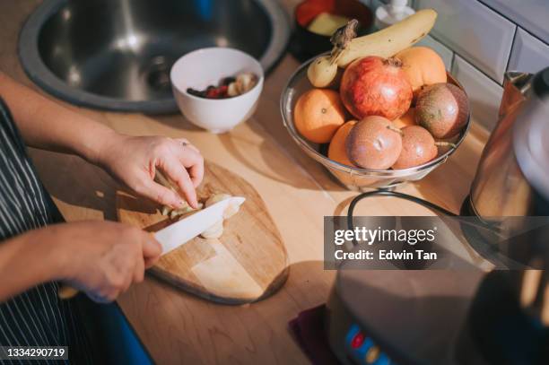 close up high angle asian chinese mid adult woman cutting banana with kitchen knife preparing morning healthy food and drink in kitchen - fruit bowl stock pictures, royalty-free photos & images