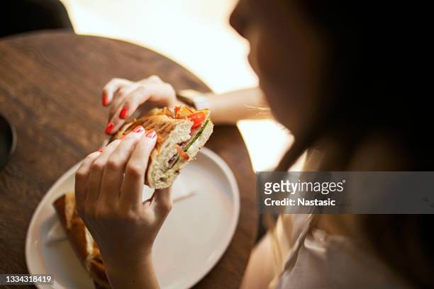 unrecognizable young woman eating a sandwich in cafe - eating fast food stock pictures, royalty-free photos & images