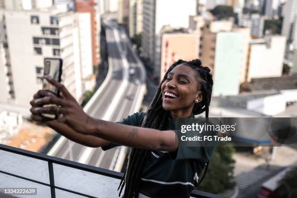 jeune femme prenant un selfie ou faisant un appel vidéo sur le balcon de l’appartement - relation à distance photos et images de collection