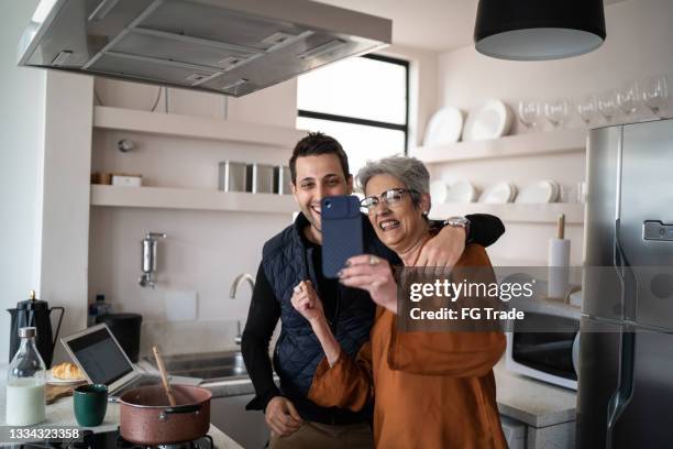 mother and son filming or doing a video call on mobile phone at home - grandmother son stock pictures, royalty-free photos & images