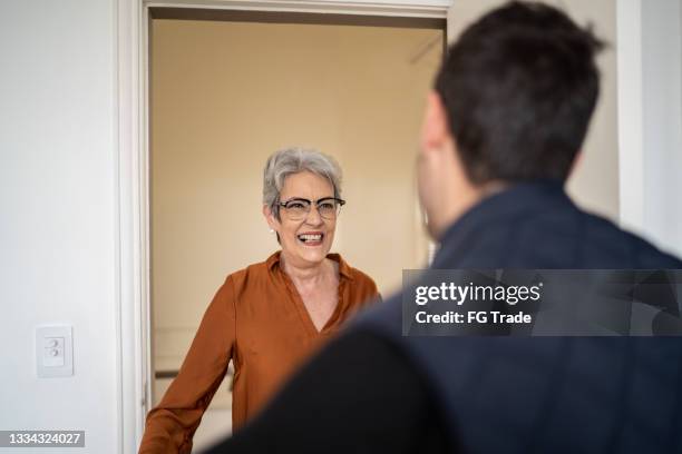 senior woman greeting son at home - apartment door open stock pictures, royalty-free photos & images